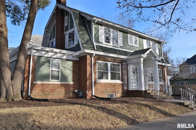 view of front of house with brick siding, roof with shingles, a chimney, a gambrel roof, and fence