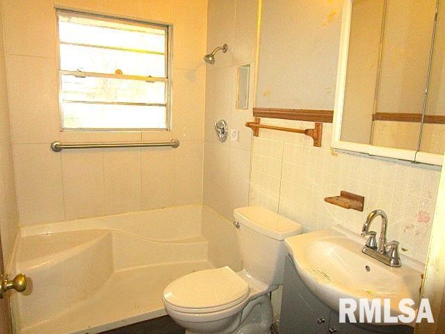 bathroom featuring decorative backsplash, toilet, walk in shower, vanity, and tile walls