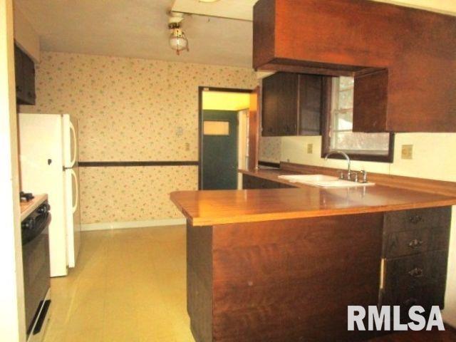 kitchen with stove, freestanding refrigerator, a sink, a peninsula, and wallpapered walls