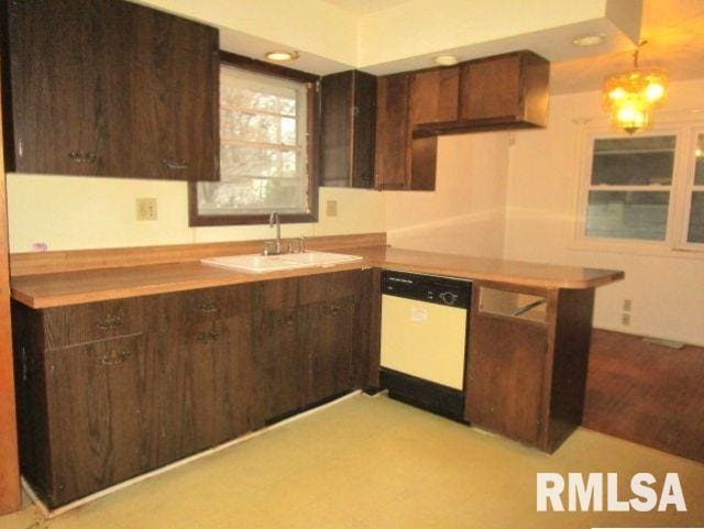 kitchen featuring white dishwasher, dark brown cabinets, a sink, and decorative light fixtures