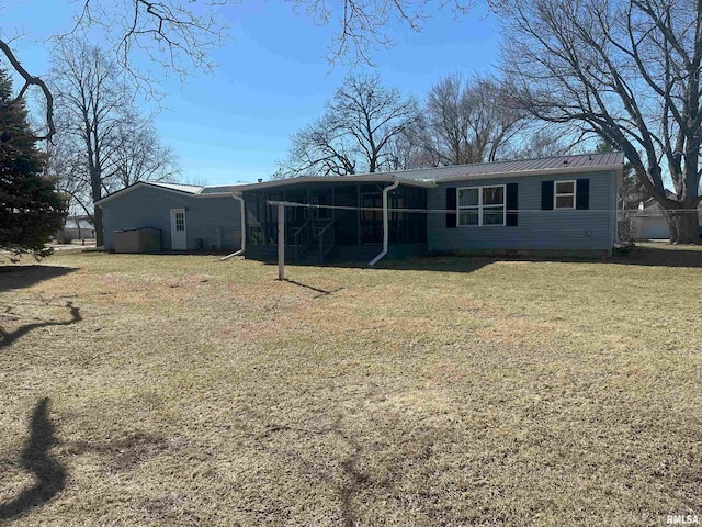 back of property featuring a sunroom, metal roof, a standing seam roof, and a lawn