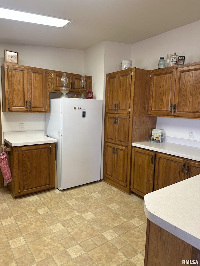 kitchen with light countertops, freestanding refrigerator, and brown cabinets