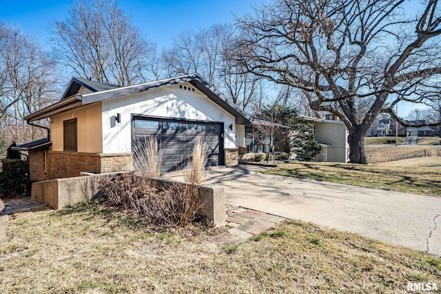 view of side of property featuring stone siding, an attached garage, concrete driveway, and a yard