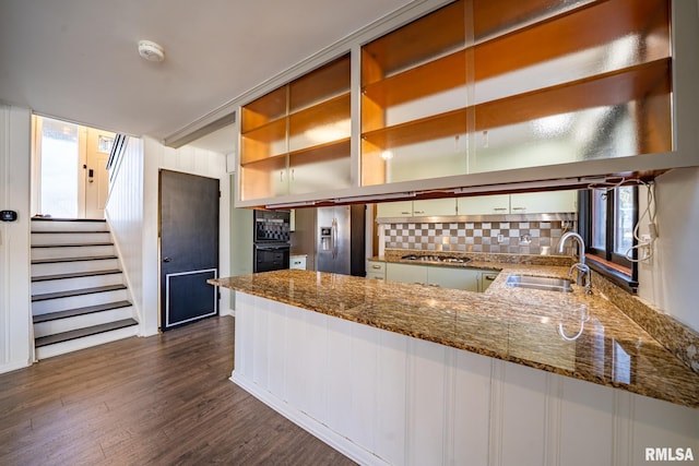 kitchen featuring a peninsula, dark stone counters, a sink, stainless steel appliances, and dark wood-type flooring