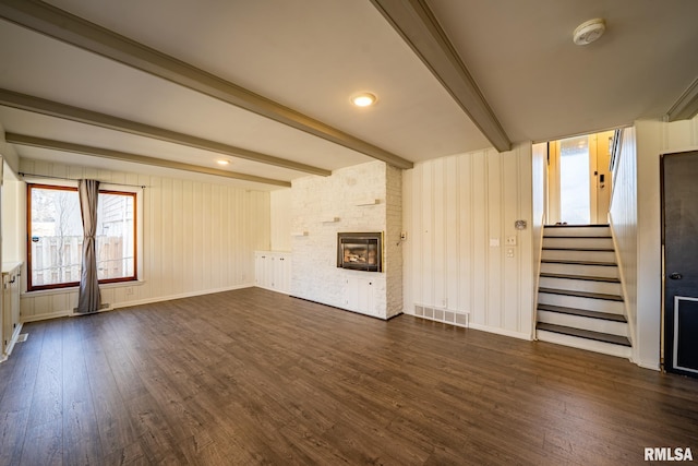 unfurnished living room featuring visible vents, beam ceiling, dark wood finished floors, stairway, and a large fireplace