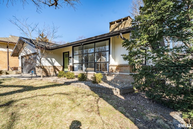 rear view of house featuring an attached garage, a lawn, and a chimney