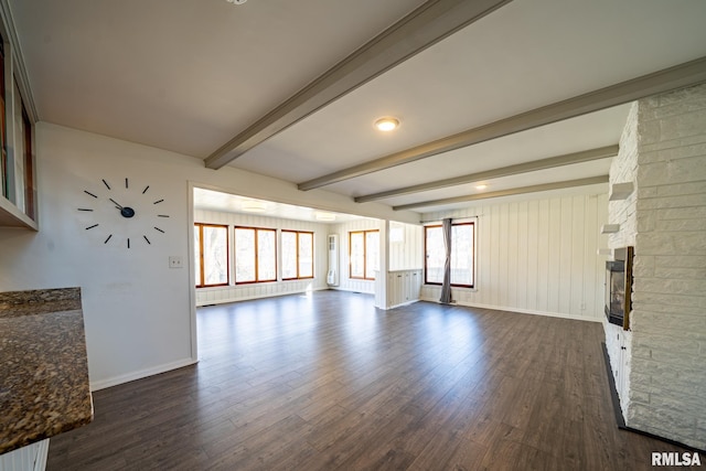 unfurnished living room featuring beamed ceiling, baseboards, dark wood finished floors, and a fireplace