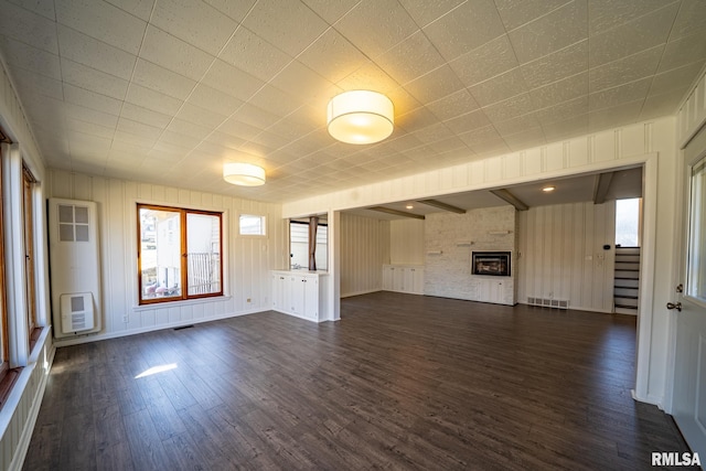 unfurnished living room with visible vents, heating unit, dark wood-style floors, stairway, and a fireplace