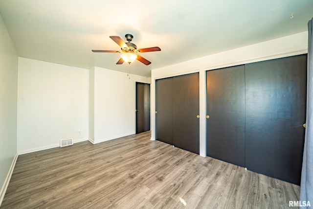 unfurnished bedroom featuring visible vents, ceiling fan, baseboards, multiple closets, and wood finished floors