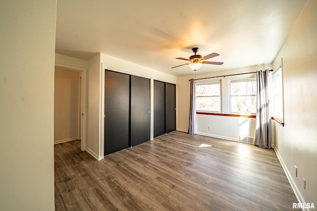 unfurnished bedroom with a ceiling fan, wood finished floors, baseboards, and two closets