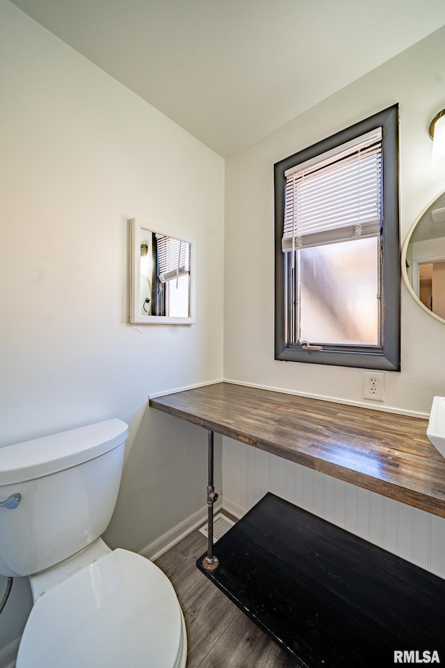 half bath featuring vanity, toilet, wood finished floors, and baseboards