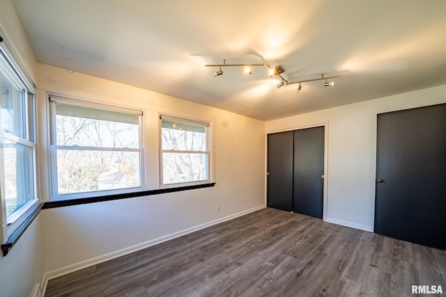 unfurnished bedroom featuring two closets, a baseboard radiator, baseboards, and dark wood-type flooring