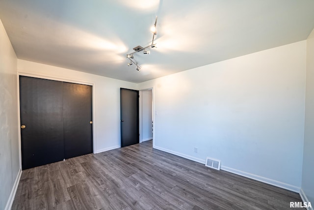 unfurnished bedroom with dark wood-style floors, visible vents, a closet, and baseboards