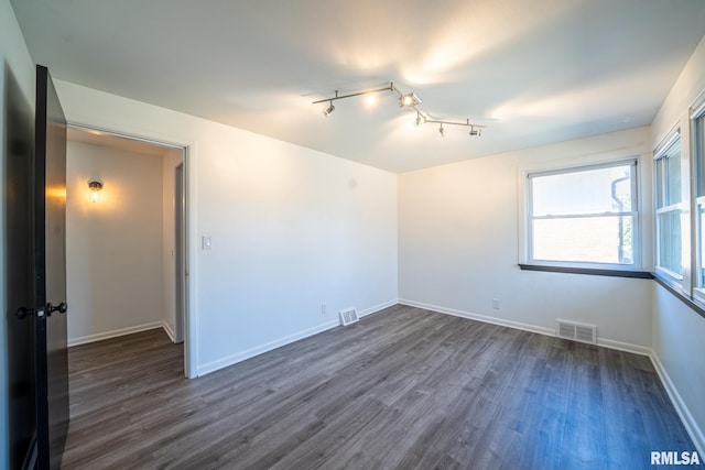 empty room featuring dark wood-style floors, visible vents, and baseboards