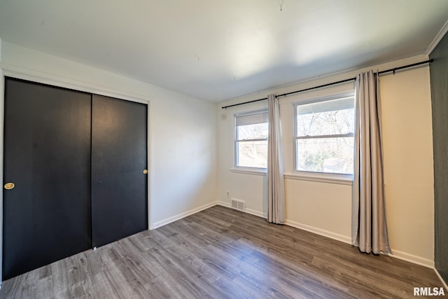 unfurnished bedroom with visible vents, baseboards, a closet, and wood finished floors