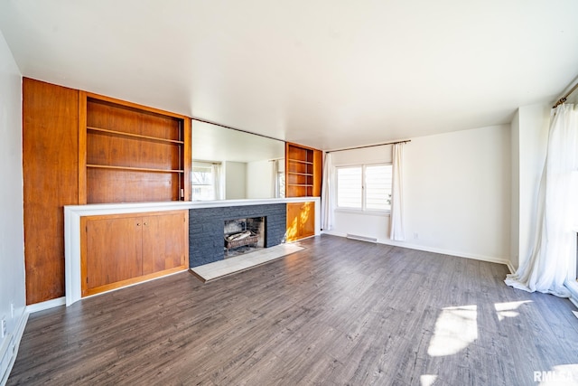 unfurnished living room with visible vents, baseboards, a brick fireplace, and dark wood-style floors