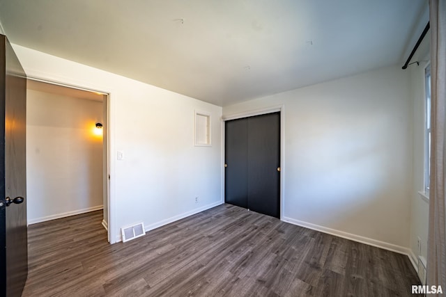 unfurnished bedroom featuring visible vents, baseboards, a closet, and dark wood finished floors