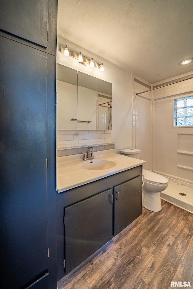 bathroom with vanity, wood finished floors, a stall shower, toilet, and backsplash