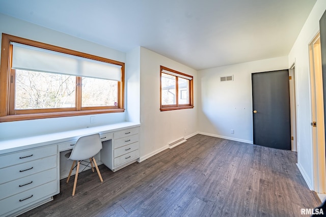 unfurnished office featuring visible vents, baseboards, dark wood-type flooring, and built in desk