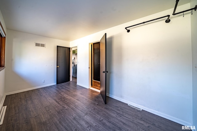 empty room featuring dark wood-style floors, visible vents, and baseboards