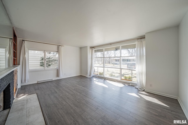 unfurnished living room with a baseboard heating unit, baseboards, wood finished floors, and a fireplace