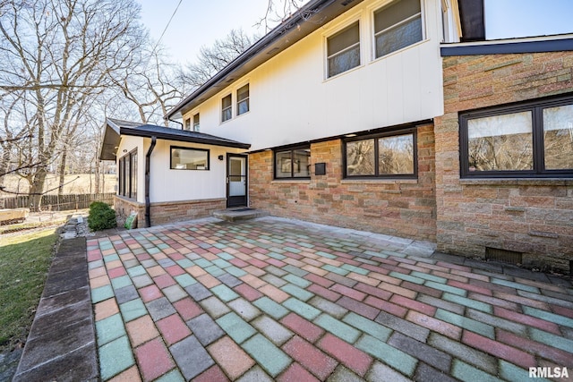 back of property with stone siding, fence, and a patio area