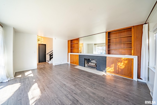 unfurnished living room featuring built in shelves, wood finished floors, stairway, a fireplace, and baseboards