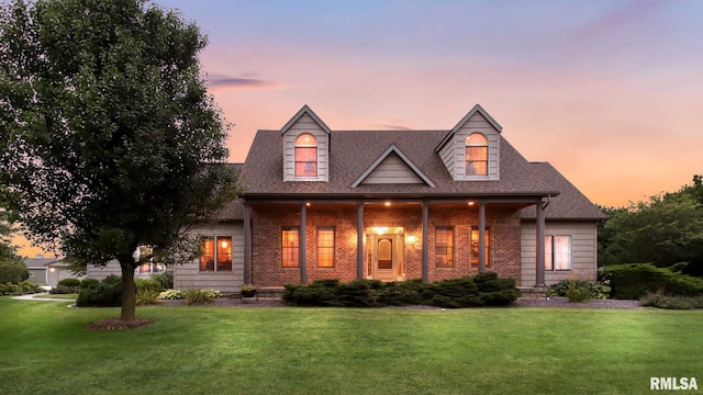 cape cod house with a shingled roof, a front lawn, and brick siding