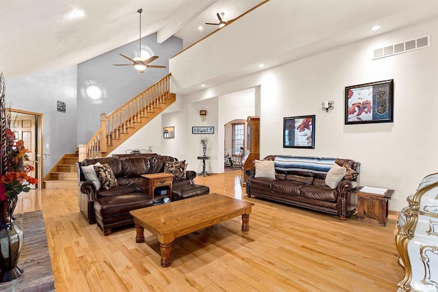 living area with arched walkways, high vaulted ceiling, visible vents, light wood-style floors, and stairs