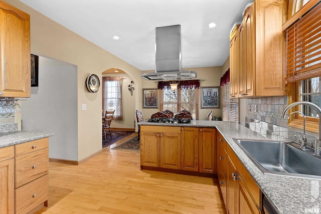 kitchen featuring arched walkways, island exhaust hood, light wood-style flooring, a sink, and a peninsula