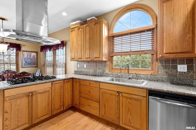 kitchen featuring light wood finished floors, appliances with stainless steel finishes, a sink, a peninsula, and wall chimney exhaust hood