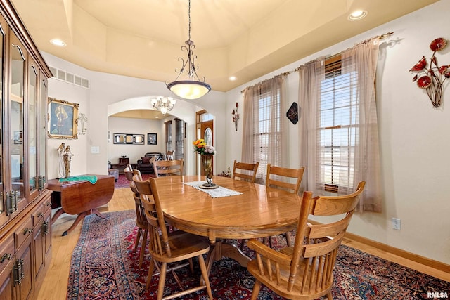 dining room featuring visible vents, arched walkways, a raised ceiling, baseboards, and light wood-style flooring