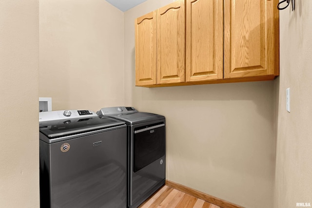 laundry area featuring cabinet space, light wood-style flooring, baseboards, and washing machine and clothes dryer