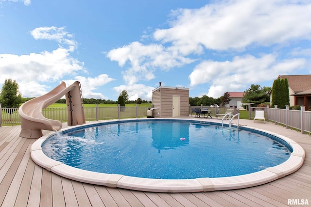 view of swimming pool with a storage shed, a water slide, an outbuilding, and fence