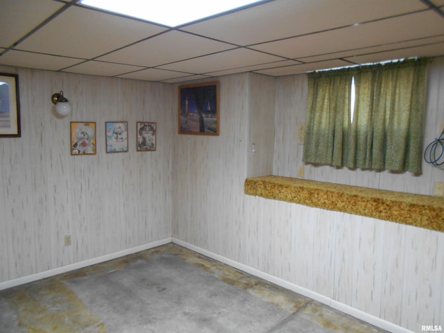 finished basement featuring wooden walls, baseboards, and a drop ceiling