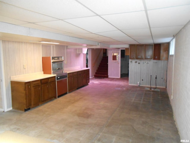 kitchen with a paneled ceiling, wooden walls, stainless steel oven, light countertops, and light floors