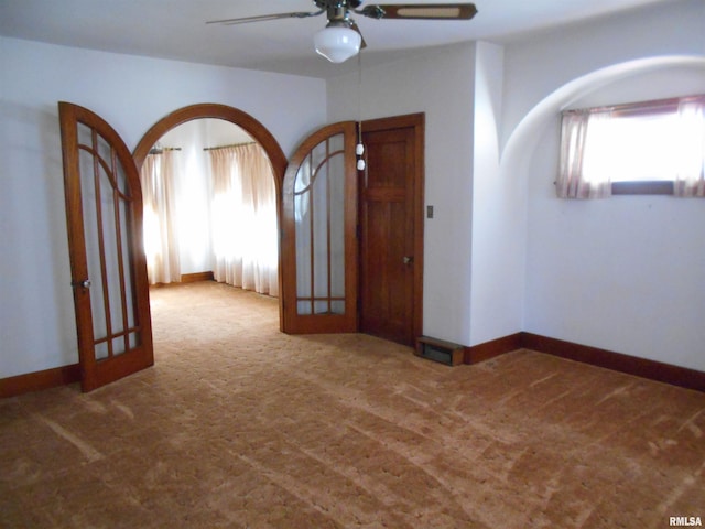 carpeted spare room featuring a wealth of natural light, arched walkways, and baseboards