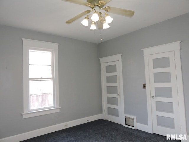 unfurnished room with dark colored carpet, visible vents, ceiling fan, and baseboards