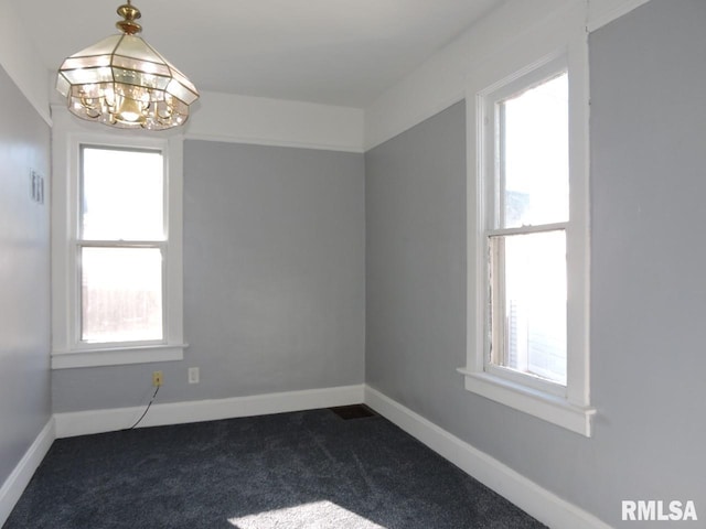 empty room featuring an inviting chandelier, plenty of natural light, and dark colored carpet