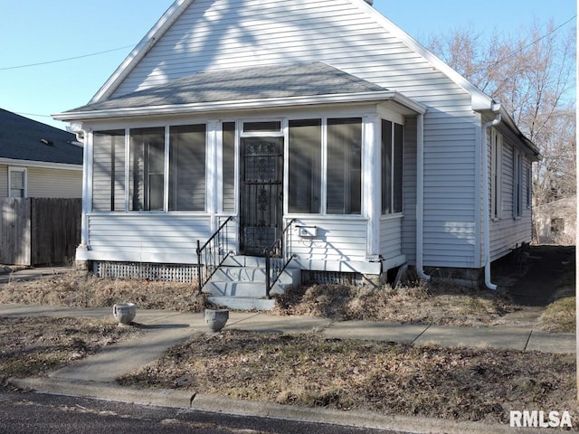 bungalow-style home featuring a shingled roof, entry steps, a sunroom, and fence