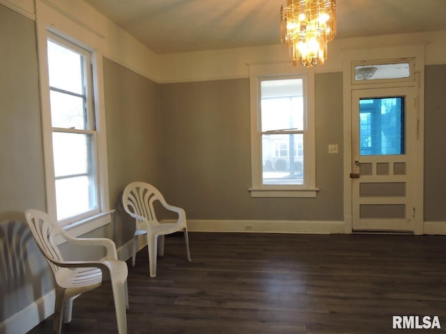 sitting room with dark wood-type flooring, baseboards, and an inviting chandelier