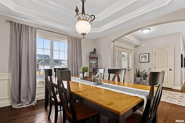 dining room featuring arched walkways, dark wood-style flooring, a tray ceiling, crown molding, and a chandelier