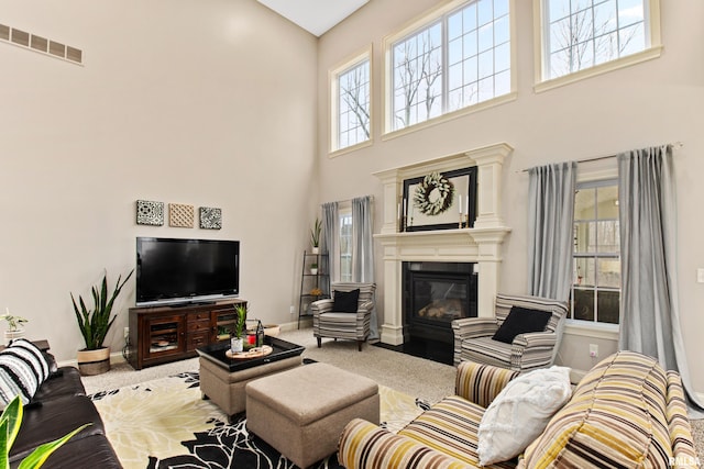 living room with a glass covered fireplace, visible vents, a towering ceiling, and baseboards