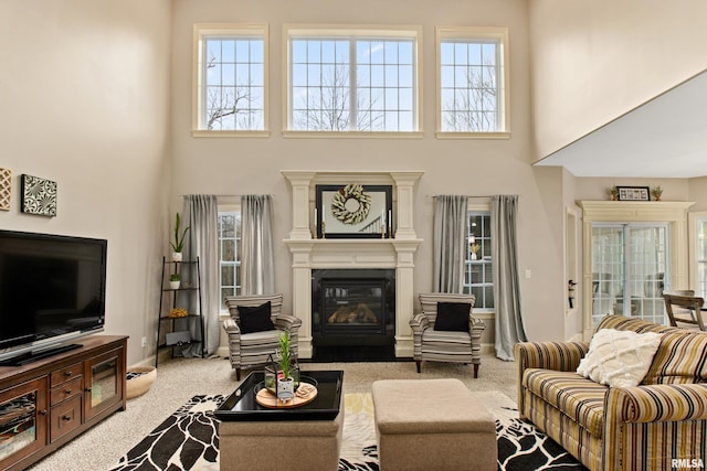 carpeted living area with a towering ceiling, baseboards, and a glass covered fireplace