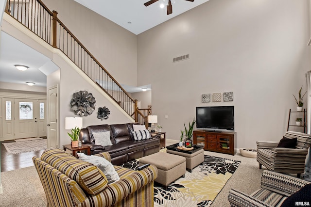 living area featuring carpet floors, visible vents, a high ceiling, ceiling fan, and stairs