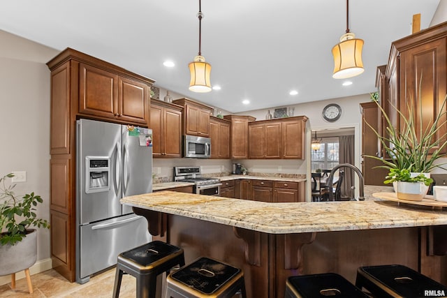 kitchen featuring a breakfast bar, stainless steel appliances, a sink, light stone countertops, and a peninsula