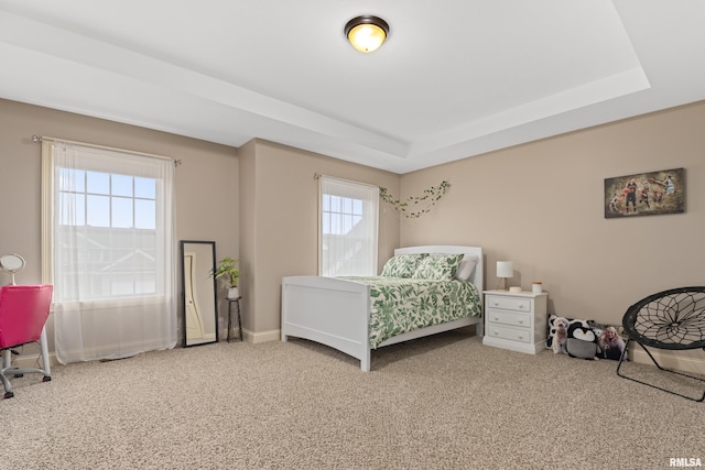 carpeted bedroom with a tray ceiling and baseboards