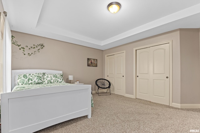 unfurnished bedroom with carpet floors, a raised ceiling, baseboards, and multiple closets