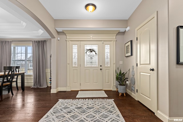 entrance foyer with arched walkways, dark wood-type flooring, crown molding, and baseboards