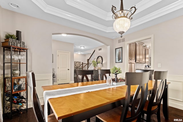 dining space with a tray ceiling, arched walkways, visible vents, a decorative wall, and wainscoting